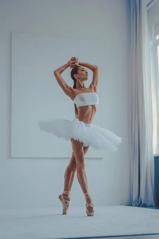 Zuza on pointe in a tutu, hands above her head, in a pale blue room