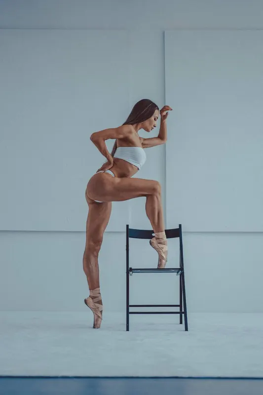Zuza standing tall beside a simple chair in a pale blue studio