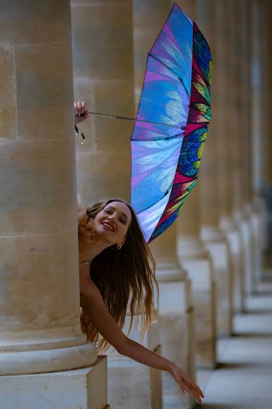 Zuza laughing as she leans out from behind a stone column with an umbrella