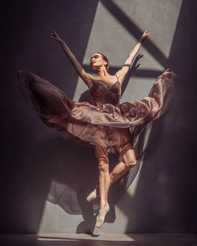 Zuza on pointe in a flowing dress, arms open in slanting light