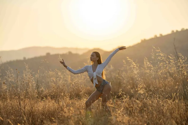 Zuza dancing in a field of tall grass with the low sun behind her