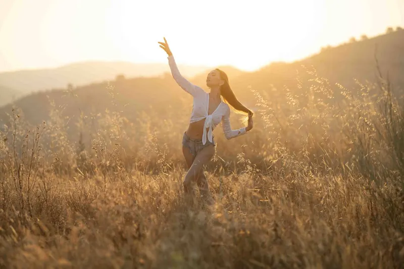 Zuza in a golden field at sunrise, one arm reaching to the sky